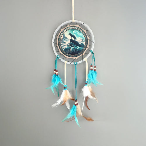 Front view of a small dreamcatcher depicting a wolf pack on a mountain, with blue, white, and brown feathers, and wooden beads.