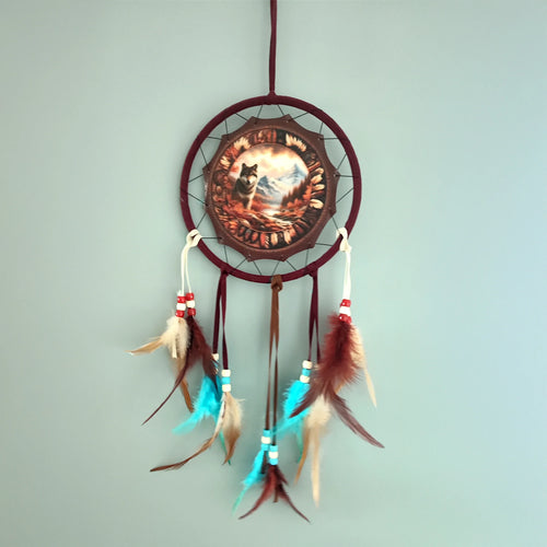 Front view of an autumnal wolf dreamcatcher with a burgundy frame, depicting a wolf in an autumn landscape, adorned with brown, cream, and turquoise feathers and colourful beads.