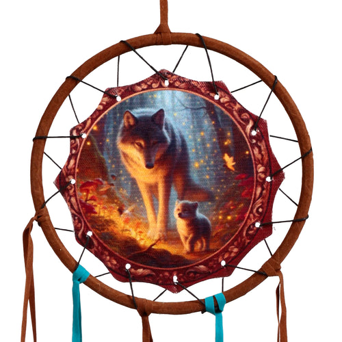 Front view of a small dreamcatcher, featuring a central fabric image of a wolf and cub in a mystical forest with glowing lights. It has a brown faux leather-wrapped circular frame with matching and turquoise fabric strips hanging below.