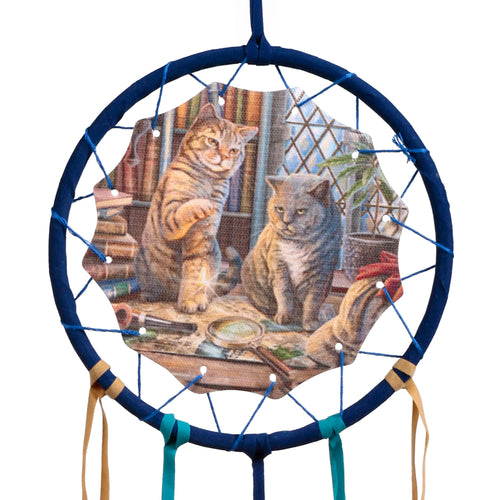 Front view of a small dreamcatcher with a dark blue hoop. It features a central Lisa Parker Purrlock Holmes cat illustration, depicting a tabby cat and a grey cat in a library setting with a magnifying glass. Blue threads form a web, and tan and teal fabric strips hang below.