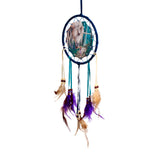 Front view of a Lisa Parker unicorn dreamcatcher, featuring a white unicorn and small fairy illustration inside a dark blue hoop, with teal and cream ribbons, wooden beads, and purple and brown feathers.