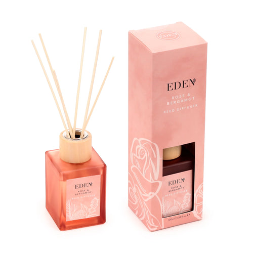 Angled view of an Eden Rose & Bergamot reed diffuser, featuring a pink glass bottle with natural reeds, alongside its matching pink gift box with botanical illustrations.