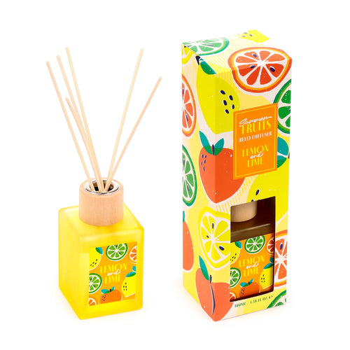 Angled view of a yellow square lemon and lime reed diffuser with natural reeds, next to its vibrant summer fruits patterned packaging box featuring a display window.