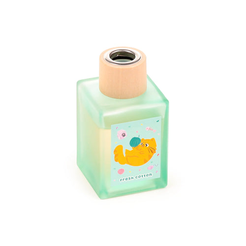 Angled view of a square frosted light green reed diffuser bottle with a wooden cap, featuring a label depicting an orange cartoon cat playing with yarn and 'fresh cotton' text.