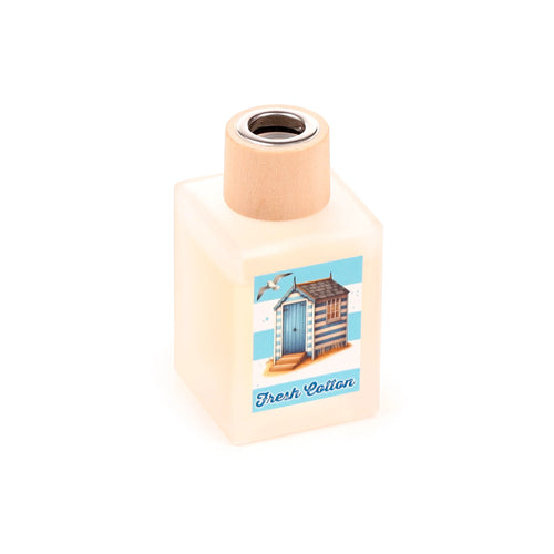 Angled view of a square, frosted glass reed diffuser bottle with a wooden-look collar and a label depicting a blue and white striped beach hut with 'Fresh Cotton' text.