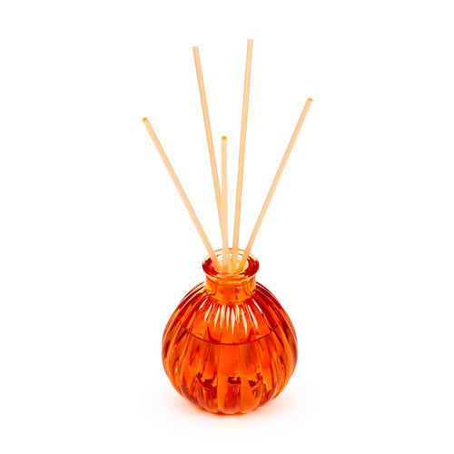 Angled view of an orange, ribbed glass reed diffuser with wooden reeds.