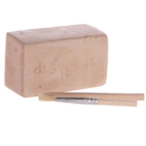 Front view of an archaeology excavation kit, featuring a light brown rectangular digging block imprinted with 'dig it out' text, accompanied by a small brush and a wooden digging tool.