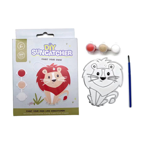 Front view of a DIY lion suncatcher craft kit on a white background. It features the product box with a lion illustration, a clear unpainted lion suncatcher outline, three pots of red, beige, and white paint, and a blue paintbrush.