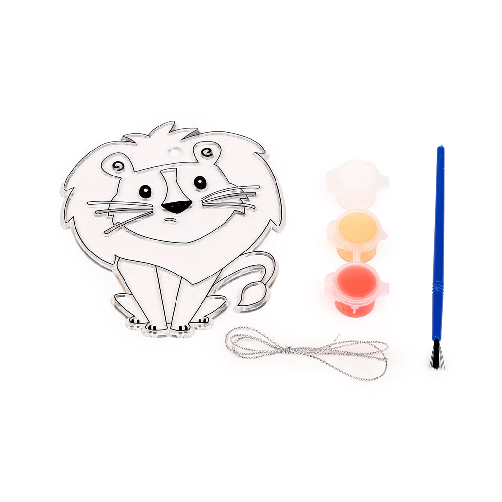 Flat lay of a DIY lion suncatcher kit, featuring an unpainted clear lion shape with black outlines, three open pots of orange, yellow, and red paint, a blue paintbrush, and coiled silver hanging string, all arranged on a white background.