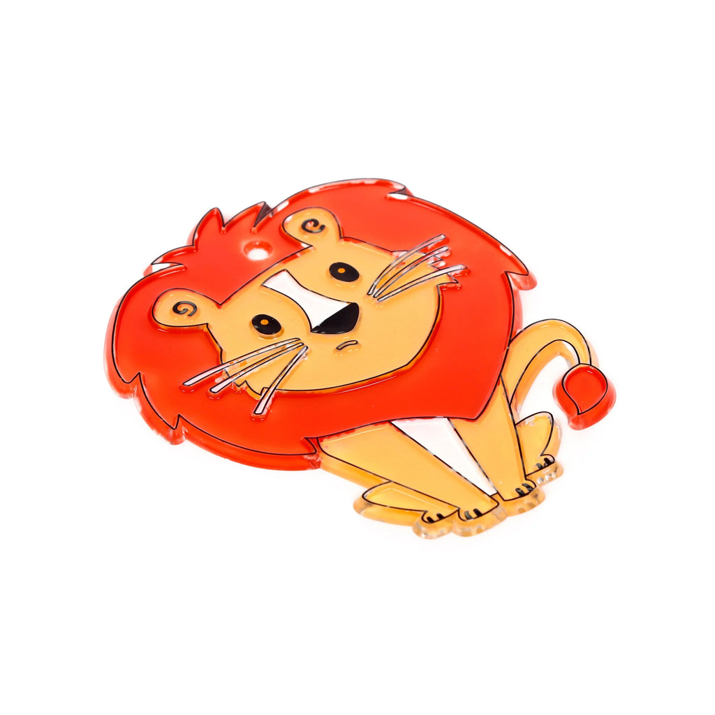 Angled view of a glossy, uncoloured DIY lion suncatcher, featuring a cartoon lion with an orange-red mane and black outlines, presented on a white background.