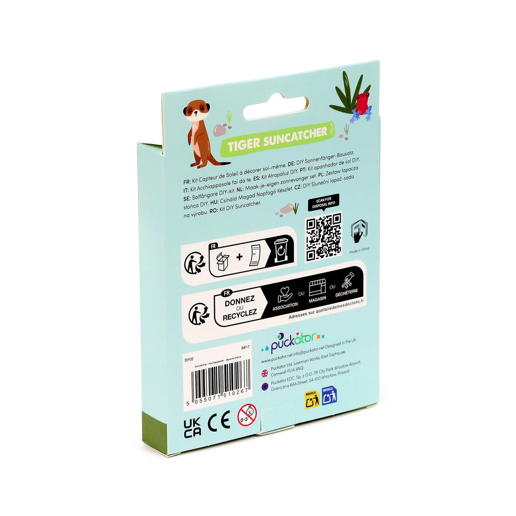 Angled view of the DIY Tiger Suncatcher kit packaging. The light blue-green box features a meerkat and red frog illustration, multilingual text for the suncatcher kit, recycling information, a barcode, and UKCA/CE safety marks.