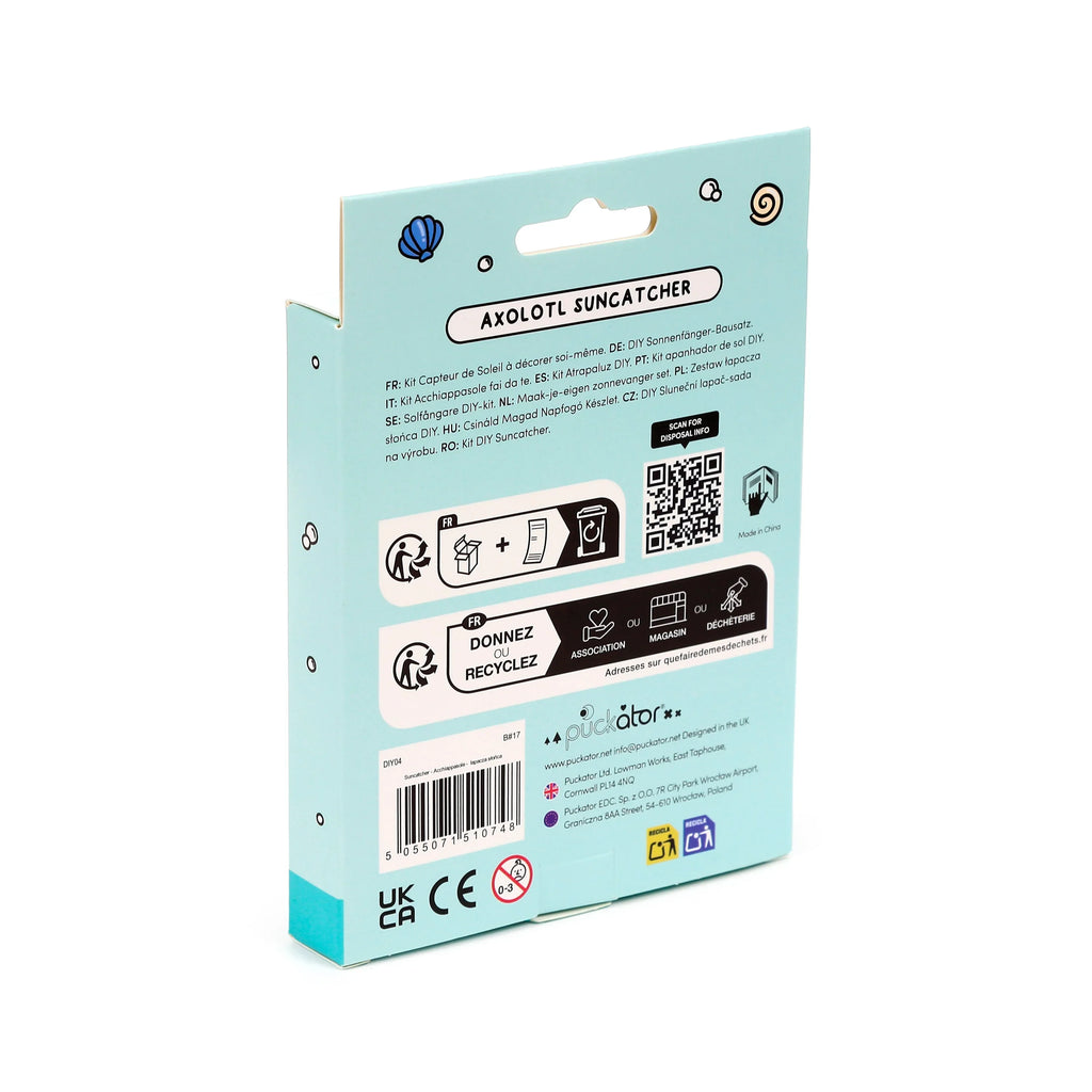 Angled view of a light blue cardboard packaging box for an Axolotl DIY Suncatcher kit, displaying multilingual product descriptions, recycling symbols, a barcode, a QR code for disposal information, and a hang tab at the top.