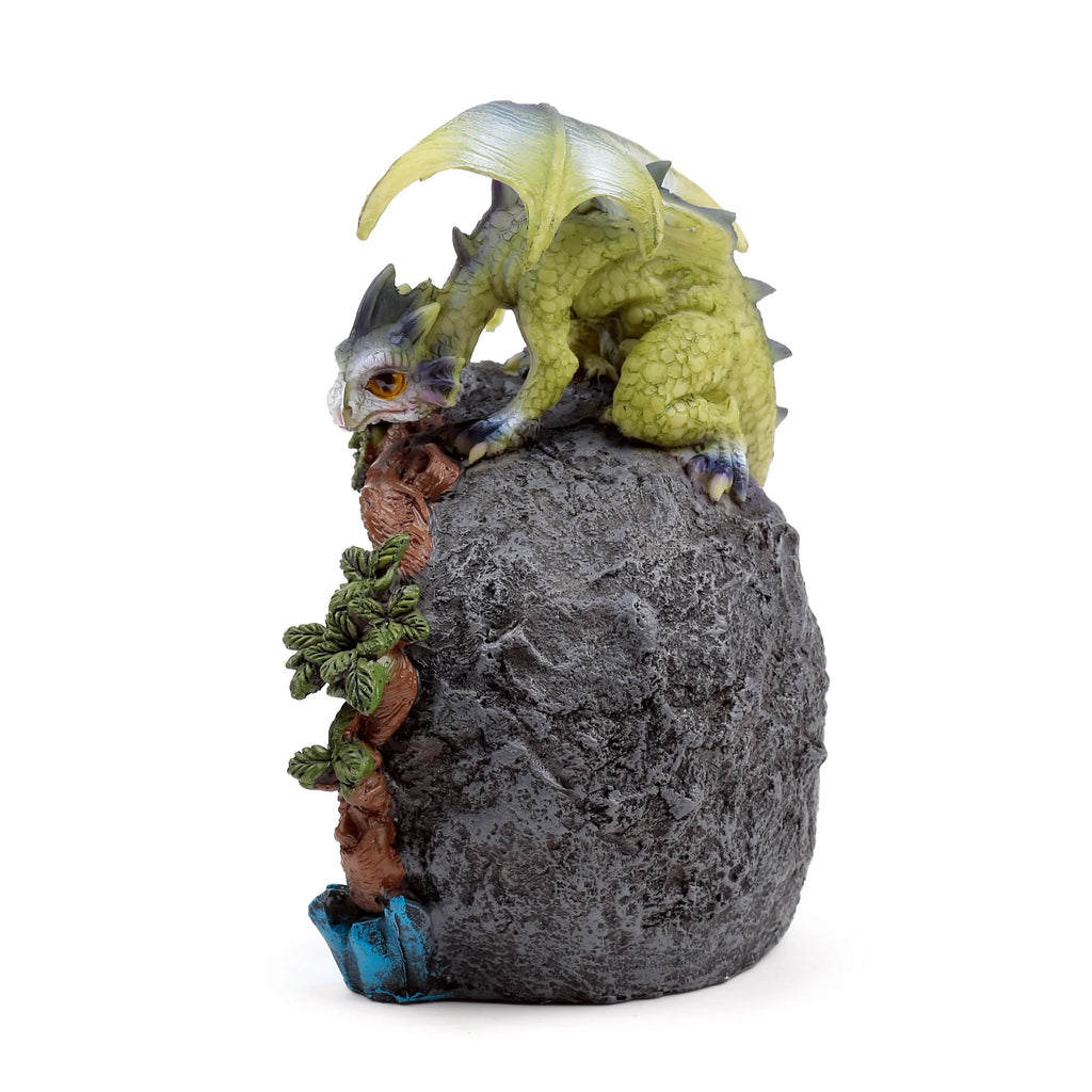 Angled view of a lime green baby dragon figurine with scales and light wings, perched on a textured dark grey rock formation with brown vines and green leaves winding up its side, and a subtle blue detail at the base.