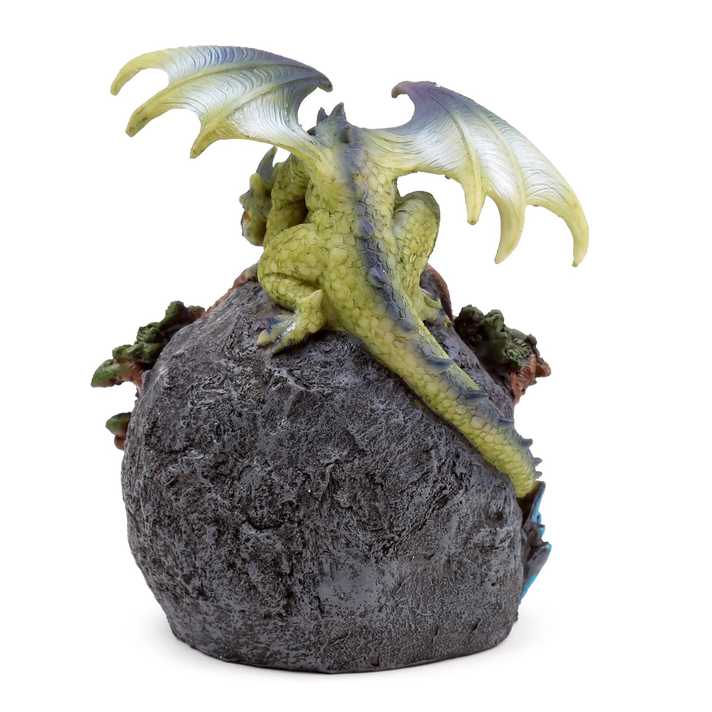 Back view of a green and yellow dragon figurine with prominent ribbed wings and purple-tinged scales, perched on a dark grey textured rock base with hints of green foliage.