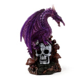 Amethyst-coloured dragon figurine perched on a white skull, resting on a dark, mossy base with brown mushrooms, viewed from a slightly angled front.