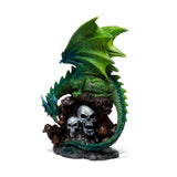 Emerald green dragon figurine with detailed scales and outstretched wings, coiled around a dark base featuring grey skulls and brown mushrooms; angled view showing the dragon's head looking towards the skulls.