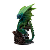 Angled view of an emerald green and blue dragon figurine, with large wings and detailed scales, perched on a dark, skull-adorned base with mushrooms, on a white background.