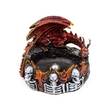 Angled view of a dark fantasy incense burner, featuring a red and gold dragon with textured wings perched above a ring of orange and black flames, with white skulls and skeleton ribs around the base and a dark central well.