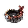 Angled view of a dark, fantasy-themed dragon incense burner, featuring a red and gold dragon with blue eyes, white skull motifs, and a silver incense cone holder within its rocky, textured bowl.