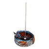 Angled view of a vibrant dragon incense burner, featuring a blue and purple scaled dragon with orange and red flame-like patterns. The dragon is coiled around a dark, circular basin, with an unlit incense stick standing upright. The burner's base displays silver-toned Celtic detailing.