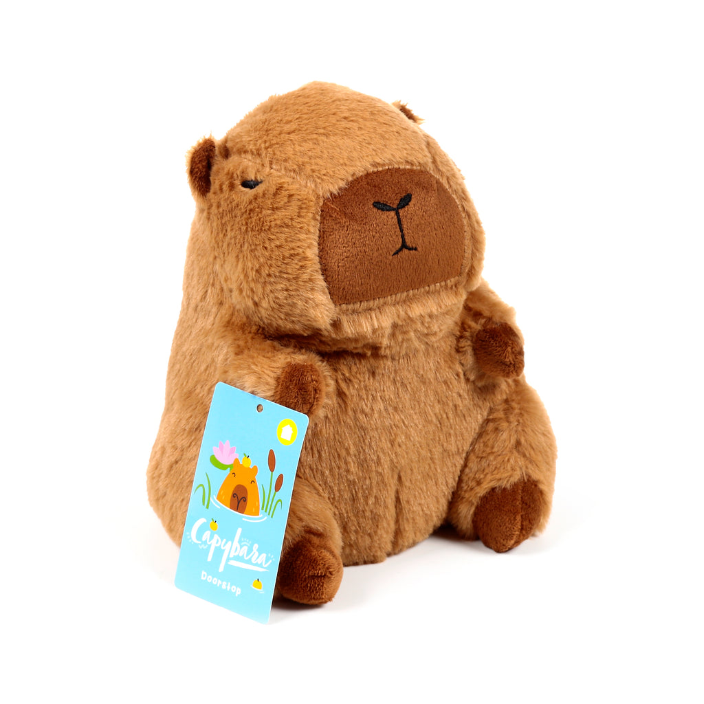 Front view of a brown plush capybara door stop, featuring embroidered sleepy eyes and a light blue product tag.
