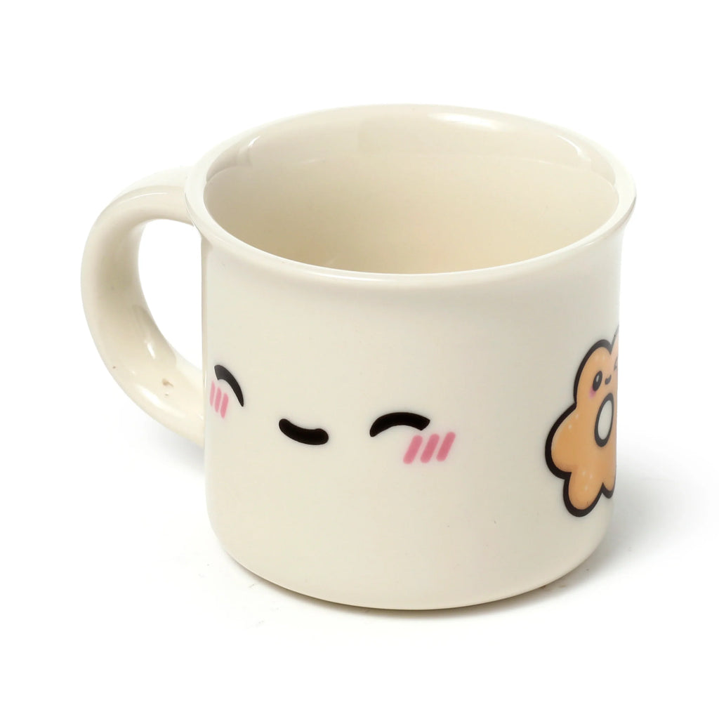 Angled front view of an off-white porcelain espresso cup, featuring a black and pink cartoon face design and part of a brown Foodiemals character, isolated on a white background.