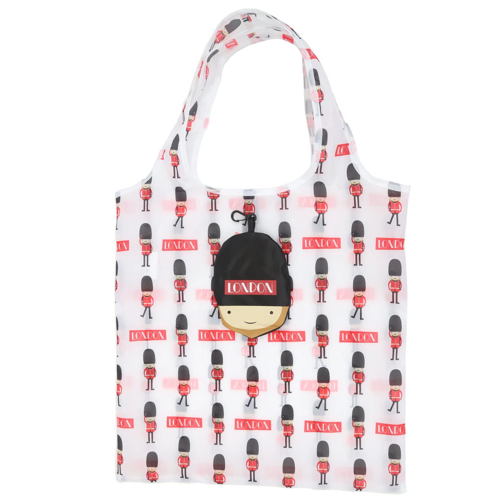 Front view of an unfolded white foldable London souvenir shopping bag with a pattern of cartoon British Guardsmen and red 'LONDON' text. A black guardsman head-shaped pouch with 'LONDON' on its hat is attached.