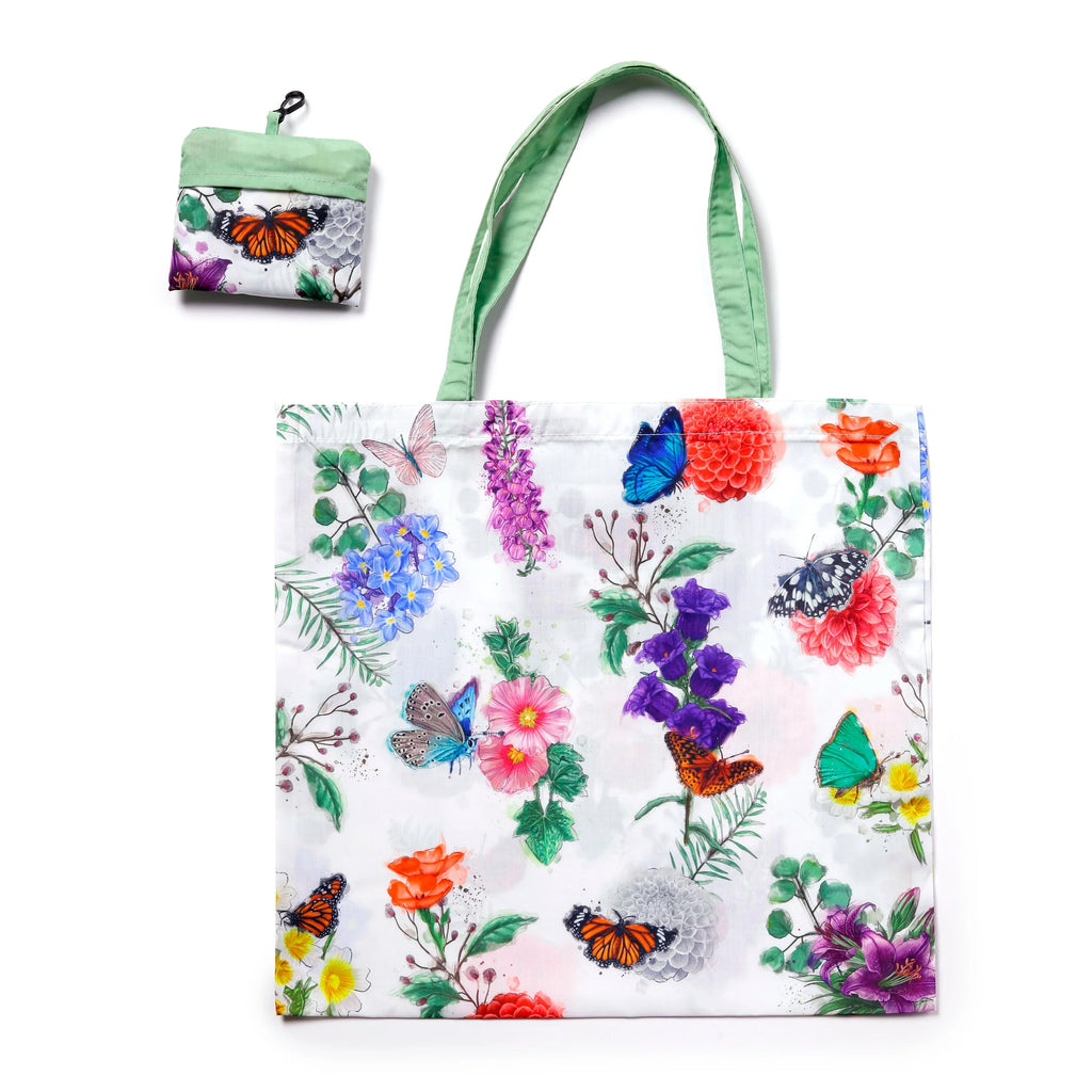 Front view of a white foldable shopping bag featuring a vibrant 'Butterfly Meadows' floral and butterfly pattern with green handles, displayed next to its compact folded form.