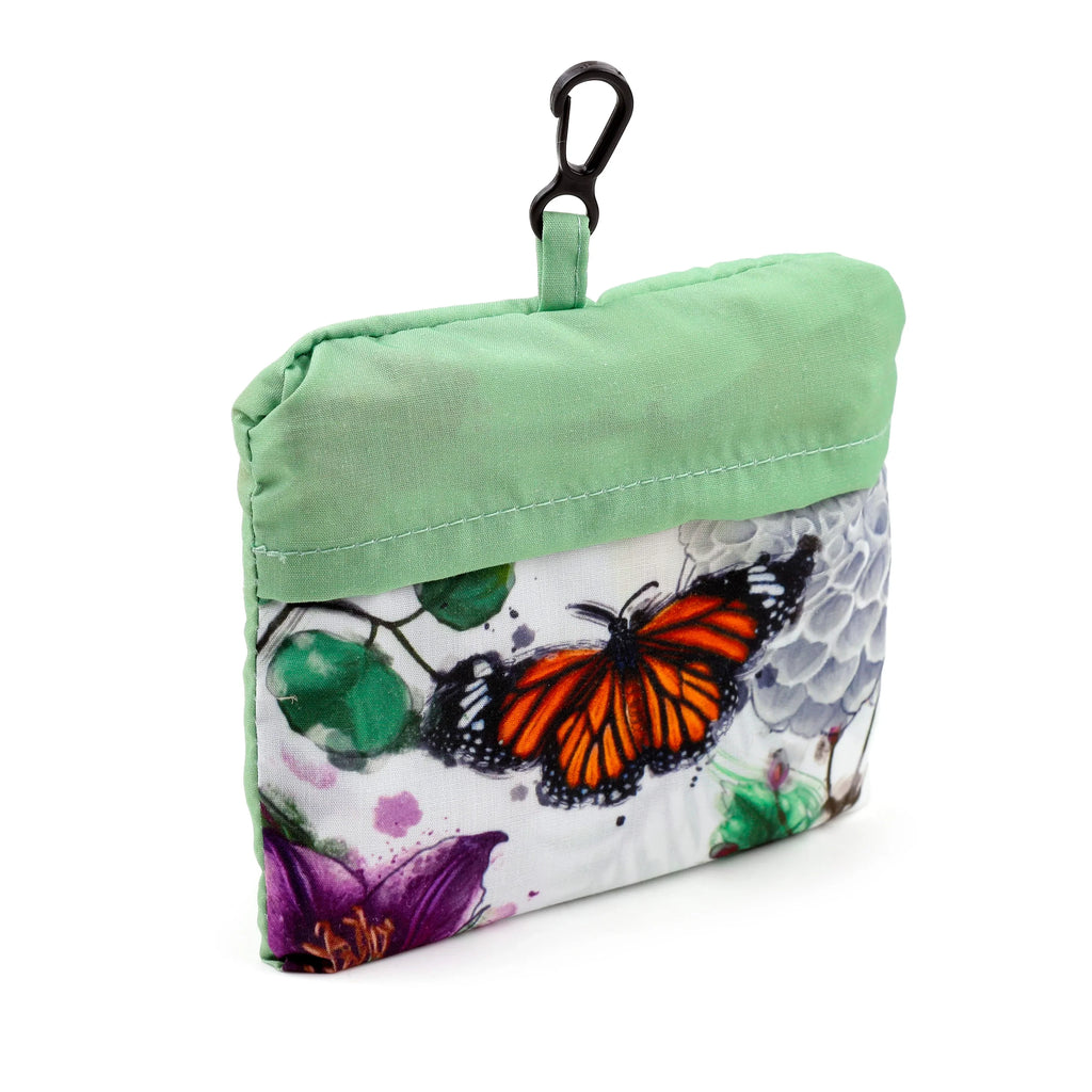 Front view of a folded shopping bag pouch featuring a vibrant orange butterfly and a floral pattern with green leaves and purple accents, topped with a light green section and a black carabiner clip, on a white background.