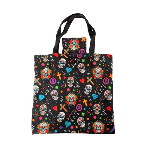 Front view of a black foldable shopping tote bag with a colourful Day of the Dead pattern, depicting sugar skulls, crosses, hearts, and diamond shapes, with black fabric handles and a small integrated pouch.