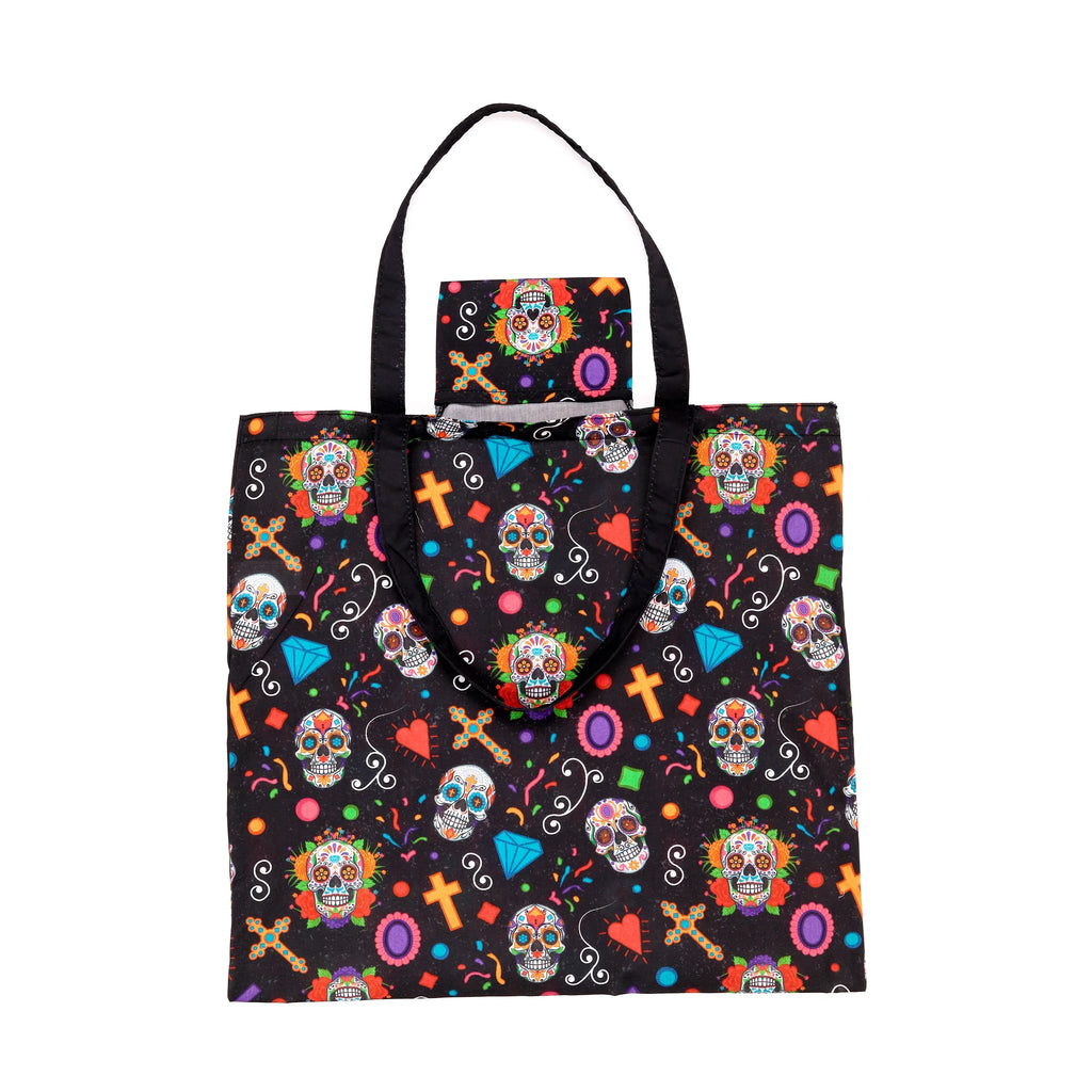 Front view of a black foldable shopping bag with a colourful Day of the Dead pattern, featuring sugar skulls, crosses, hearts, and diamonds. It has black fabric handles and a small top flap with a matching skull design.