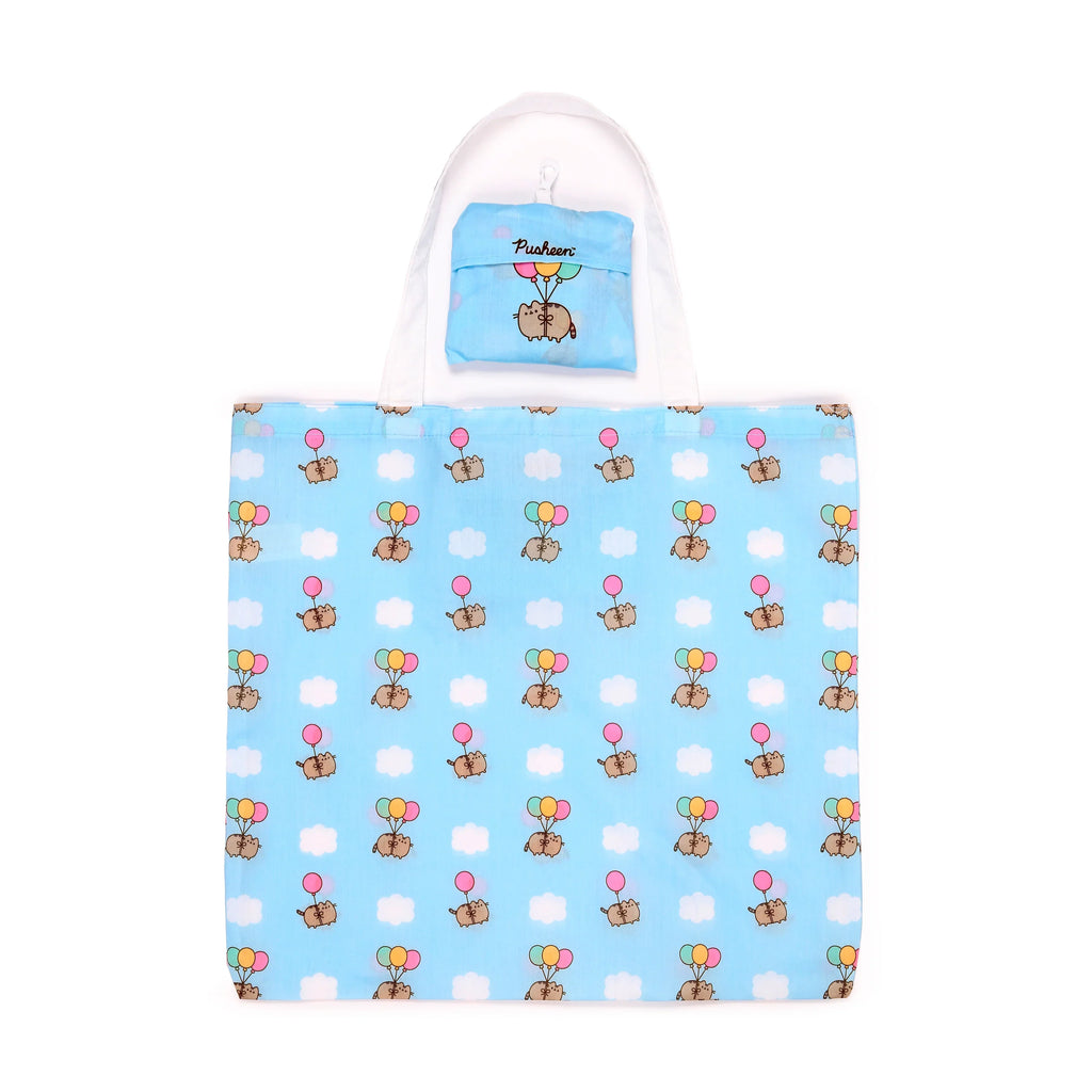 Front view of a light blue foldable shopping tote bag featuring a pattern of Pusheen the cat floating with multicolour balloons amongst white clouds, with a smaller, folded pouch attached.