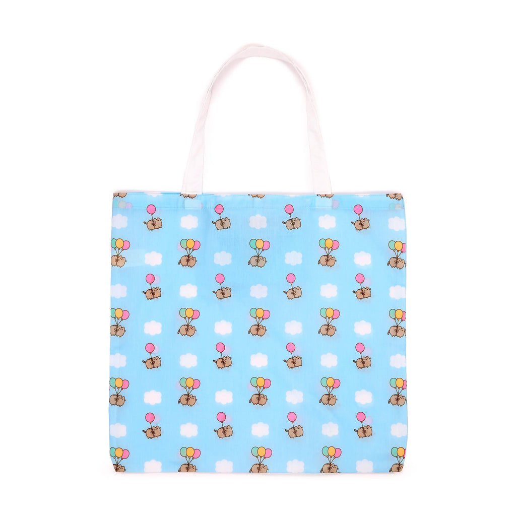 Front view of a blue shopping tote bag with white handles, patterned with cartoon cats holding colourful balloons and white clouds.
