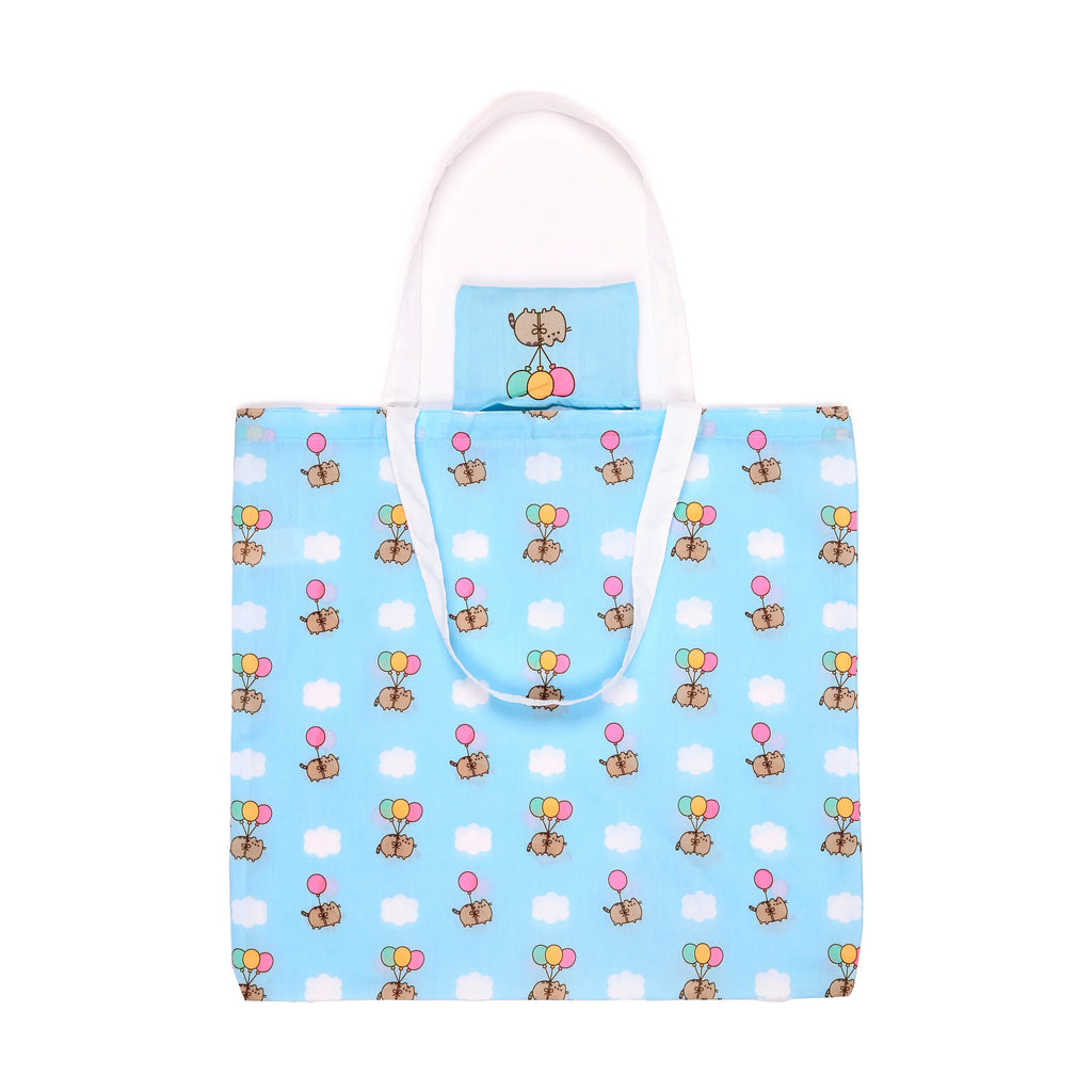 Front view of a light blue foldable shopping tote bag with white handles, featuring a repeating pattern of Pusheen the Cat holding pink, mint green, and yellow balloons, interspersed with white clouds.