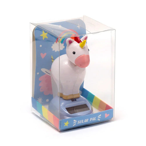 Front-side view of a 'Solar Pal - Unicorn Magic' toy in its clear plastic packaging, featuring a white unicorn figure with a yellow horn and pink nose on a light blue solar-powered base. The packaging includes a blue background insert with rainbow and heart patterns, and a rainbow-striped border at the bottom.