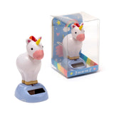 Front and side view of two unicorn 'Solar Pal' figures. One white unicorn with a pink snout, yellow horn, and colorful mane stands on a light blue base with a solar panel. The second, identical unicorn is in clear packaging with a rainbow and cloud design.