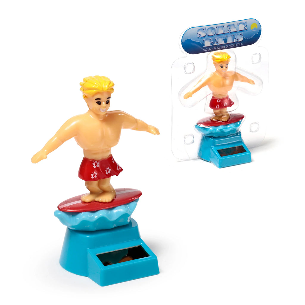 Angled view of an unboxed Solar Pal Surger Dude, a blond-haired male surfer figurine wearing red shorts with white flowers, balancing on a red surfboard over a blue wave and base with a solar panel. An identical packaged figure is visible behind it.