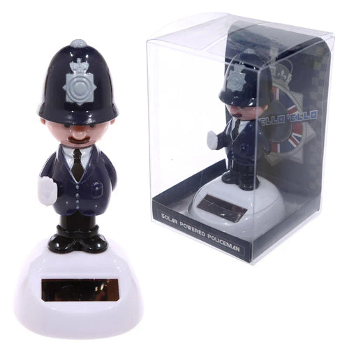 Front view of a Policeman Solar Pal figurine in a dark blue uniform with a British police helmet and raised left hand, standing on a white solar-powered base. An identical figurine is visible in clear plastic packaging in the background.