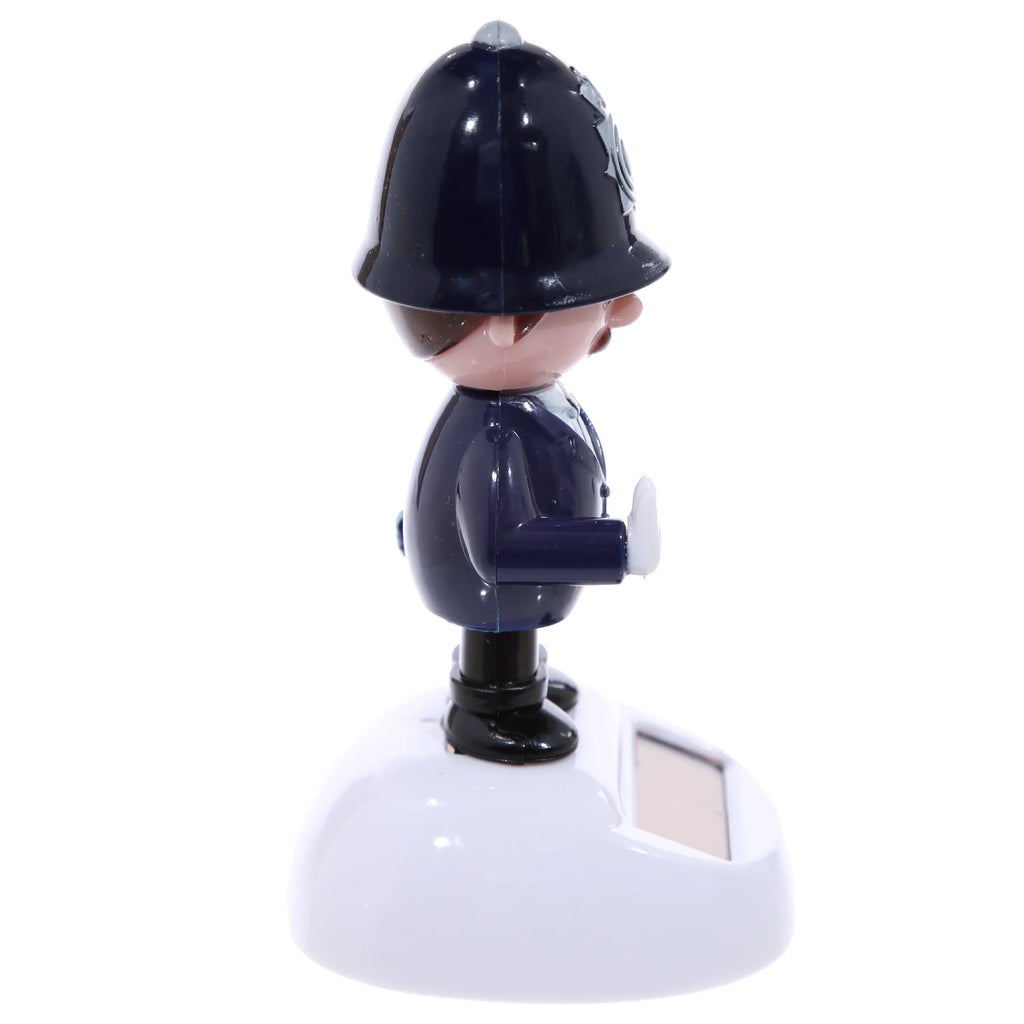 Angled side view of a Policeman Solar Pal figurine, showing the character in a dark blue uniform, black boots, and traditional police helmet with a grey badge. The figure has a brown face with a small moustache and a white hand raised. It stands on a white base with a visible solar panel.
