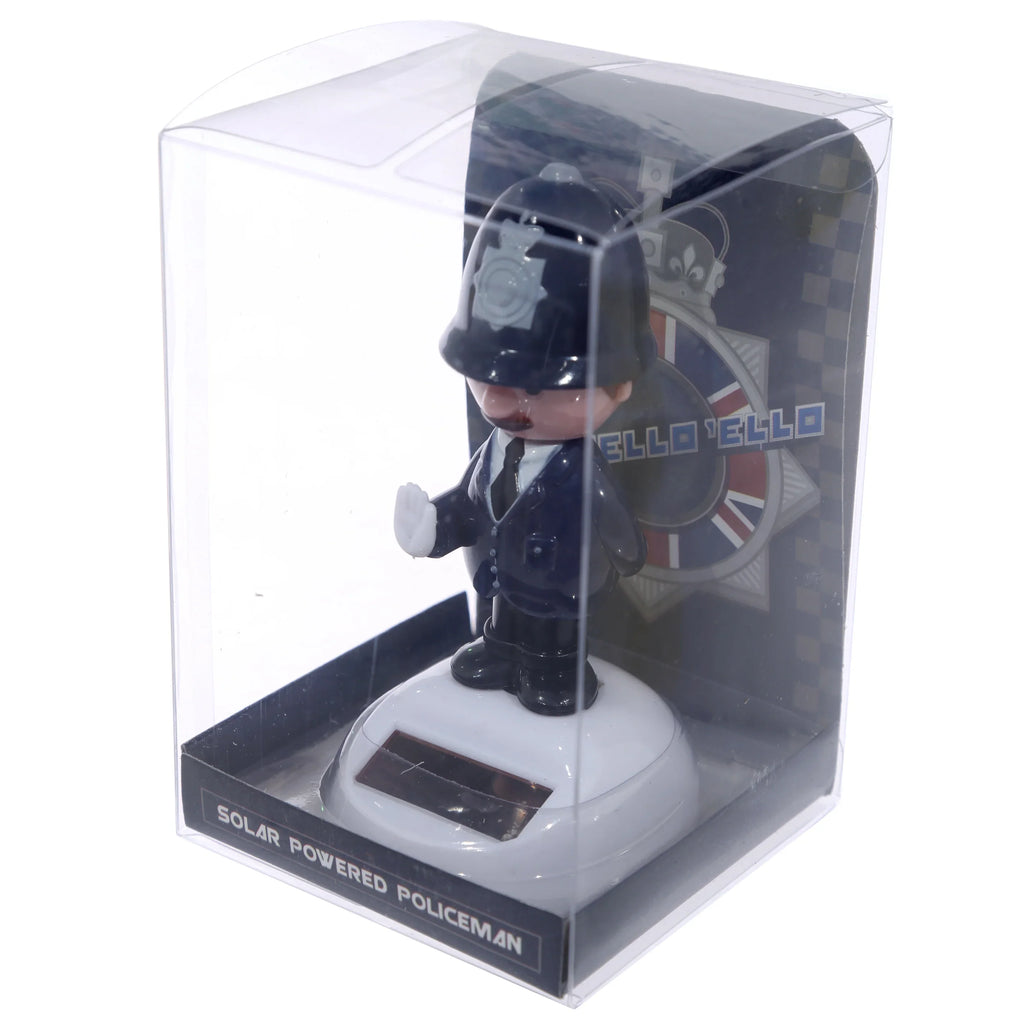 Angled front view of a Policeman Solar Pal, a small figure in a dark blue British police uniform and bobby helmet, with a raised hand, visible within clear plastic retail packaging showing its white solar-panelled base.