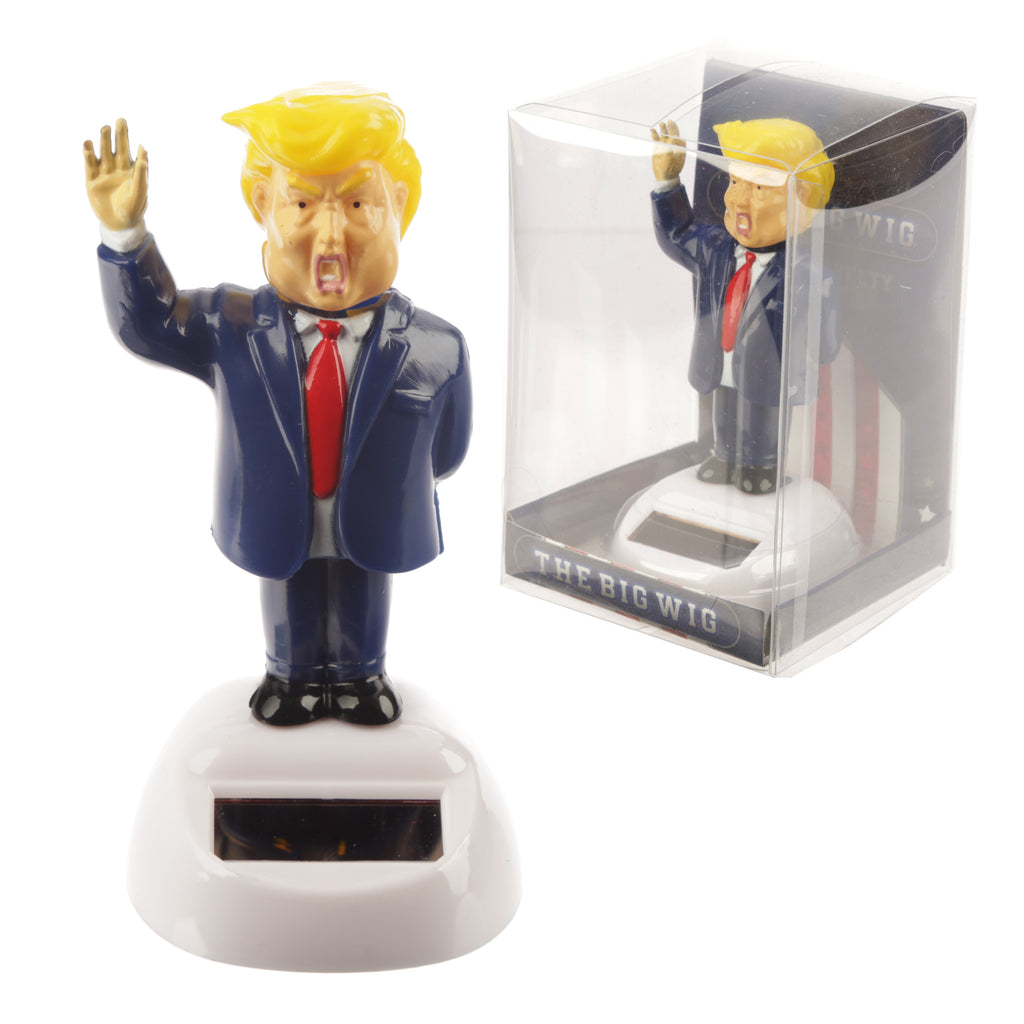 Front view of a collectable President solar pal figurine, featuring yellow hair, a blue suit, a red tie, and a raised hand, on a white base with an integrated solar panel. An identical figurine is visible in clear plastic packaging to the right.