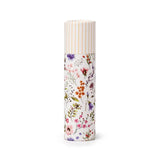 Front view of a cylindrical solid perfumed stick balm for lips. It features a white background with a vibrant wildflower meadow pattern and a white cap with thin vertical gold stripes.