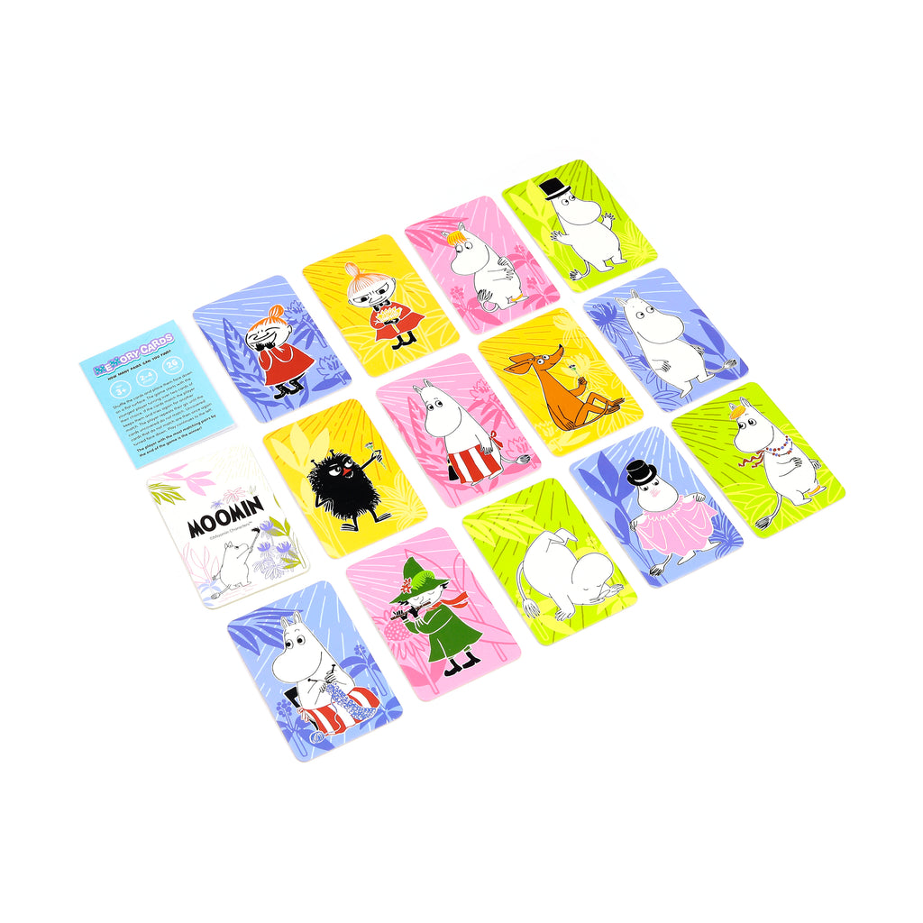Angled view from above of a children's Moomin memory card set, displaying numerous colourful rectangular cards. Each card features a distinct Moomin character against yellow, pink, blue, or lime green backgrounds, alongside a visible instruction card outlining the game rules.