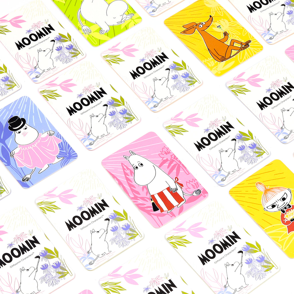 Overhead view of multiple Moomin memory game cards, featuring various Moomin characters and colourful illustrations on different pastel backgrounds, spread across a white surface.