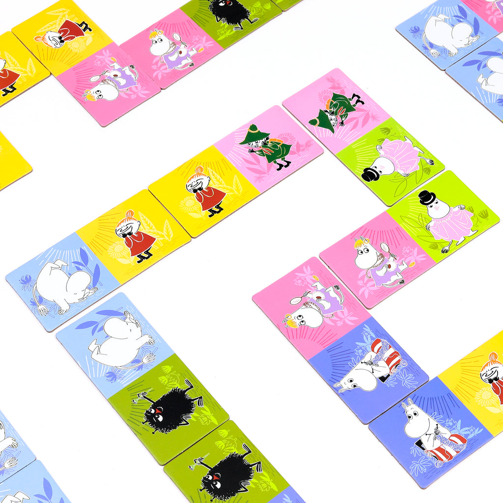 Overhead view of a Moomin picture dominoes set, showing brightly coloured tiles with various Moomin characters and subtle patterns, arranged in a winding line on a white background.