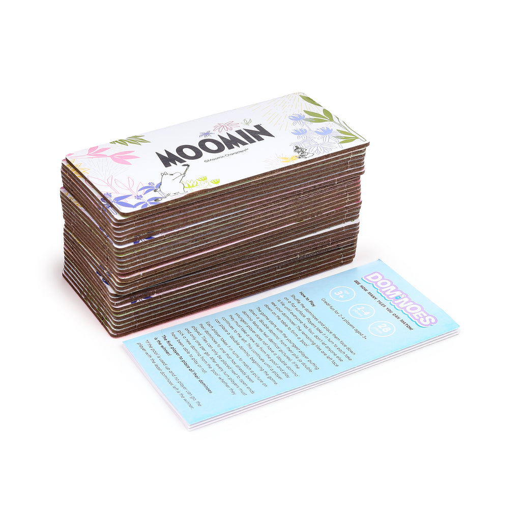Angled view of a Moomin picture dominoes set, featuring a stack of tiles with character illustrations and floral patterns on the top, next to a light blue instruction card showing game rules, age 3+, players, and pieces information.