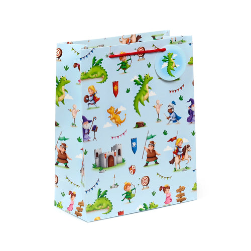 Angled view of a large, light blue gift bag with red braided handles, patterned with cartoon knights, dragons, a castle, and a wizard, featuring a circular dragon tag.