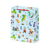 Angled view of a large, light blue gift bag with red cord handles. The bag is decorated with a detailed knights and dragons pattern, depicting various green and orange dragons, knights, princesses, wizards, and a castle. A round tag showing a green dragon is attached to one handle.