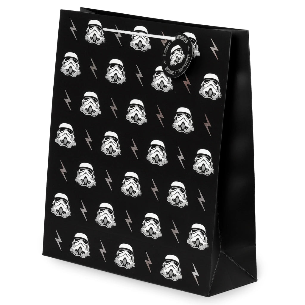 Front angled view of a black gift bag with white rope handles, featuring a repeating pattern of white Stormtrooper helmets and grey lightning bolts, and a circular tag that reads 'Original Stormtrooper'.