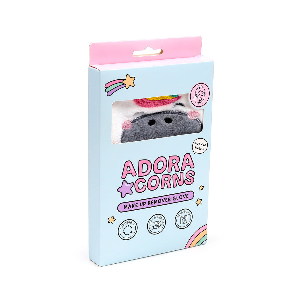 Angled view of a light blue packaged makeup remover glove, featuring a fluffy grey unicorn design with rainbow colouring visible through the box window. The packaging displays 'Adoracorns' branding and icons for 'reusable', 'soft & gentle', and 'washable'.